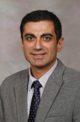 headshot of Amir, wearing a grey suit, smiling
