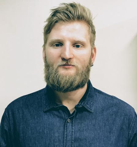 headshot of Arthur, wearing denim button up, smiling