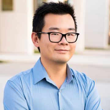 headshot of William Wang from the shoulders up in a light blue collared shirt and black rimmed glasses, smiling